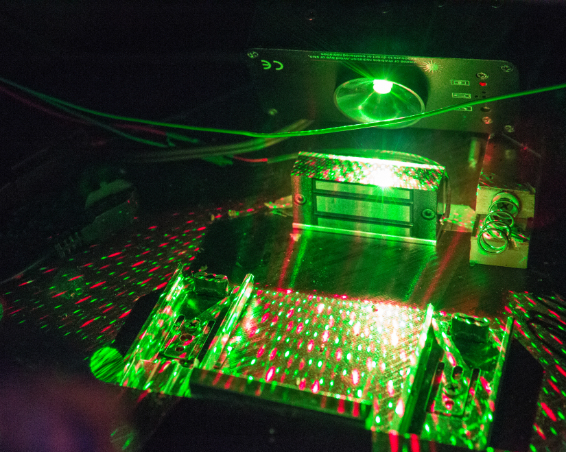 A projector shinging an array of green and red dots against a mirror. Wires, springs, magnets, and other mechanisms surround the projector.