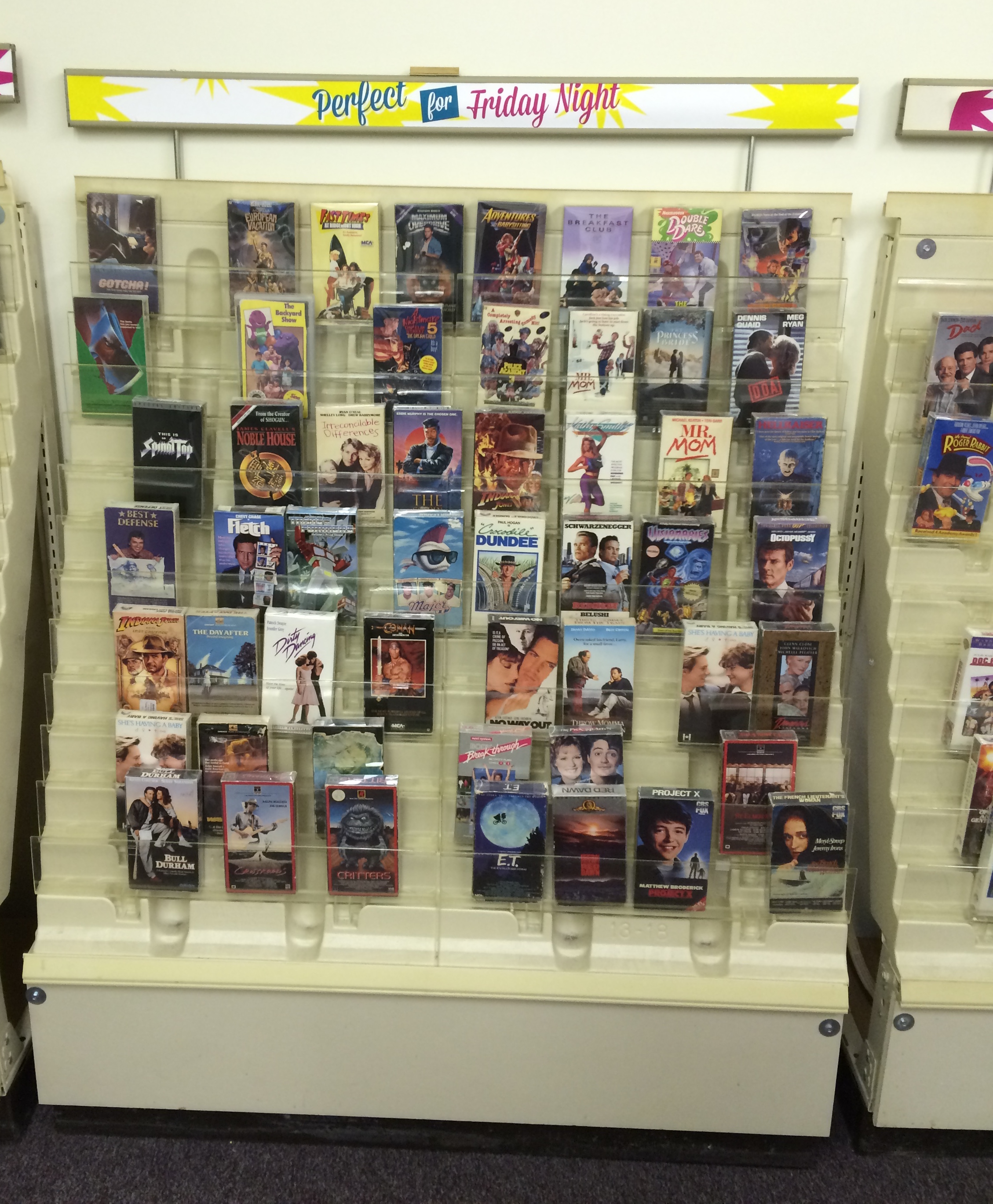 A video rental shelf containing a variety of 1980s classics movies, and some that aren't quite so classic.