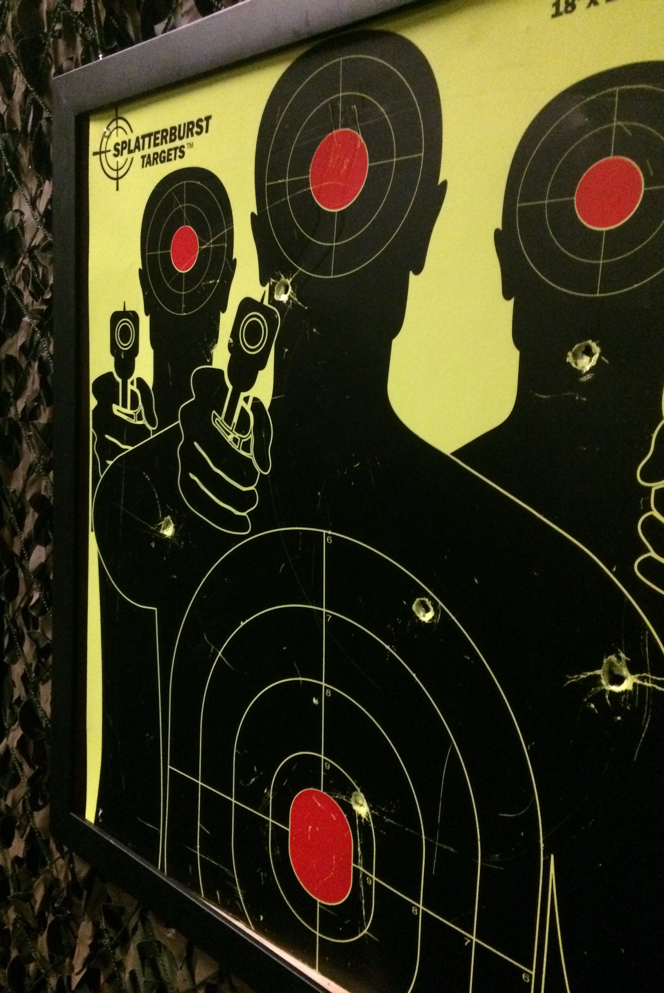 Photo of a shooting target. The target depicts the silhouette of three men with pistols. The target has a number of bullet holes in it.