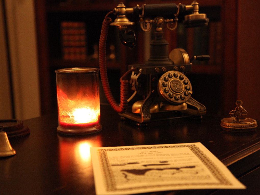 Image of a old-looking telephone and an ink-smeared letter, all lit by a candle.