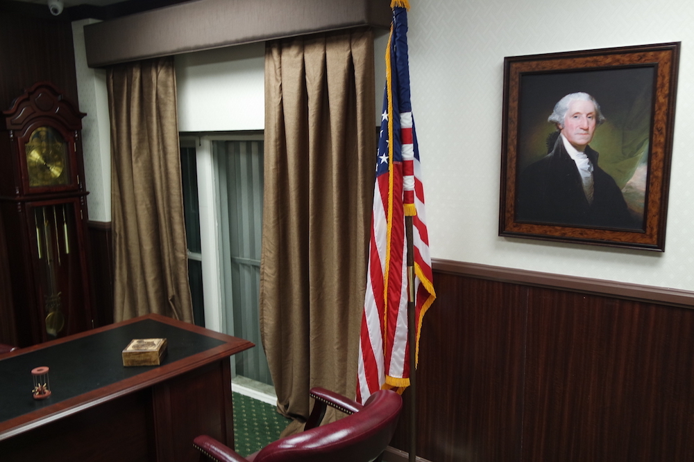 An escape room designed to look like a senator's office, complete with George Washington portrait, American flag, desk, leaver chairs, and grandfather clock.