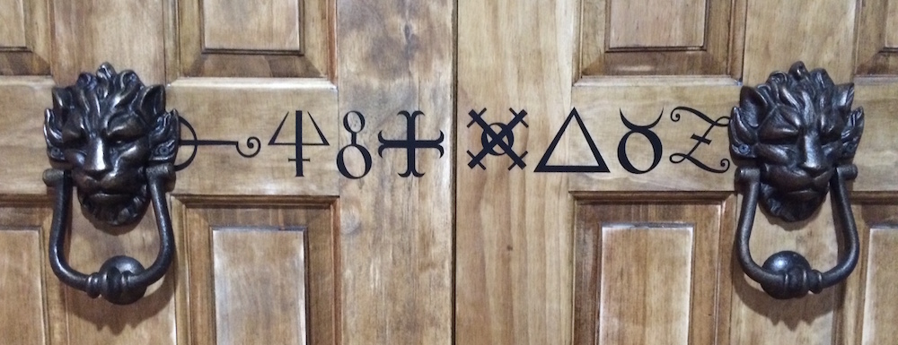 Double wood doors with runs painted on them, beset by a pair of black lion door knockers.