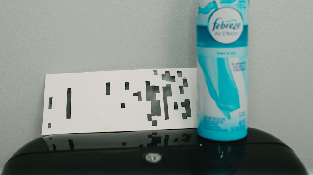 A paper overlay with slits cut in it resting atop a papertowel dispenser, next to a bottle of Febreze air freshener.