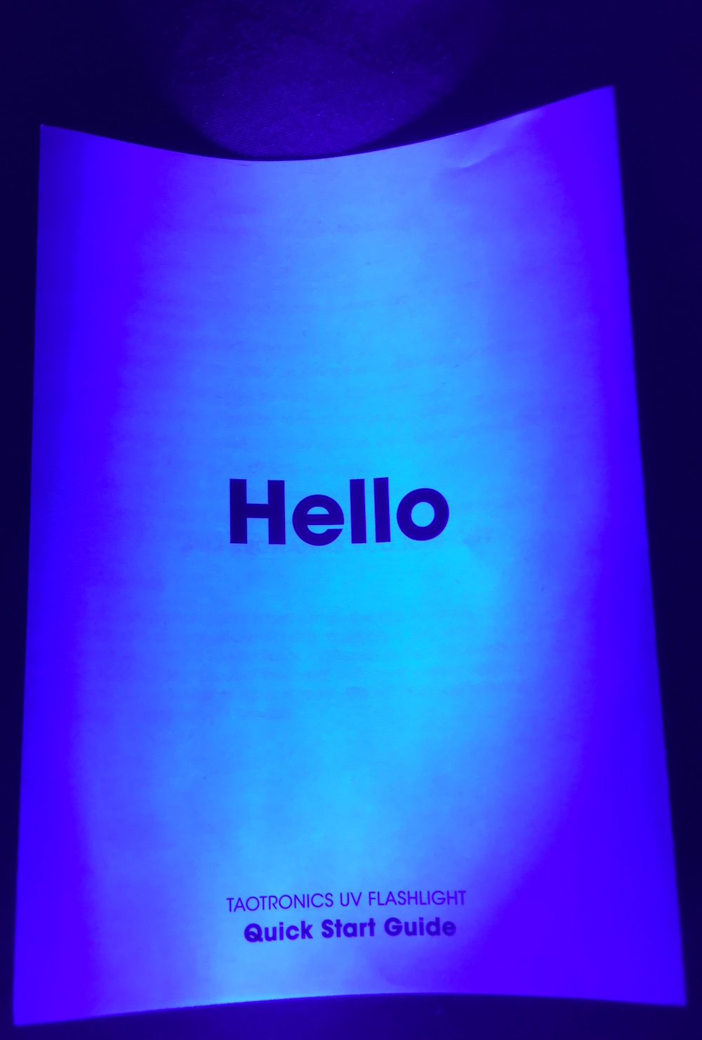 The cover of the blacklight's instructions illuminated by the blacklight. It reads, "Hello. Taotronics UV Flashlight. Quick Start Quide."