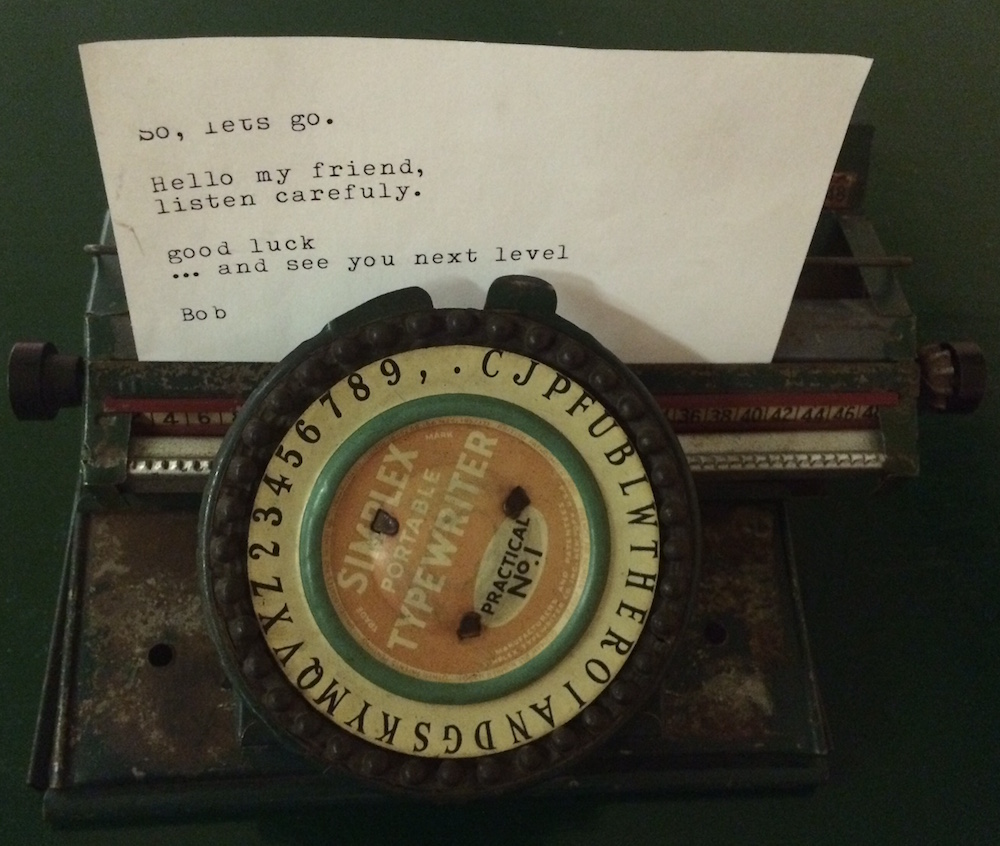 An old portable typewriter with a typed letter in it. It reads, "So, let's go. Hello my friend, listen carefuly. good luck ... and see you next level Bob"