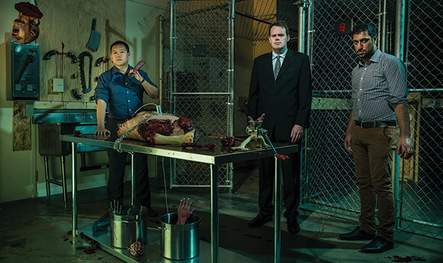 Photo of Edwin and his partners in one of their horror games. It's dark and there are body parts as well as implements of destruction postioned throughout the room.