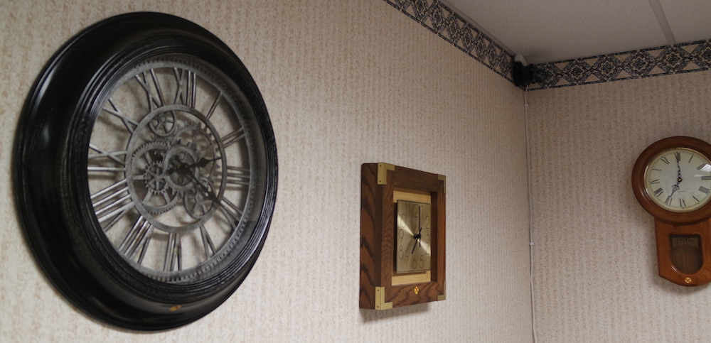 A bland wall with a number of differnt clocks hanging on it.