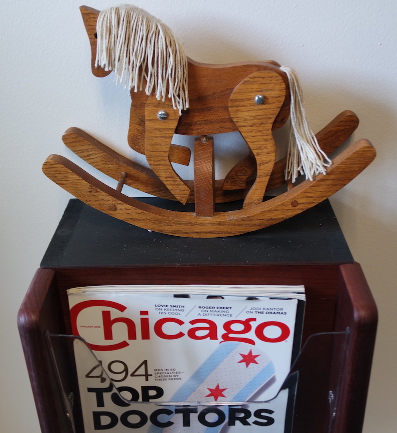 A small rocking hourse resting atop a magazine rack containing the 