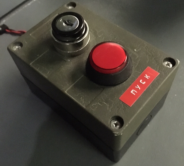 Close up of a big red button with a keyway next to it. There is a label with Russian written on it.