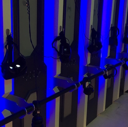 In-game, a glowing blue wall with a series of Oculus Rift headsets hanging from it.