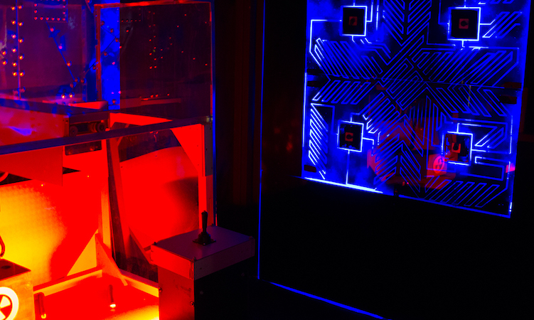 In-game, a non-repeating pattern appears illuminated in blue in the background, a cube with a joystick is illumminated in red in the foreground.