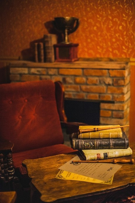 A big red chair beside a small desk with wands and wizarding books.