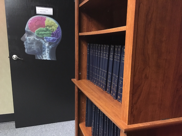 In-game: A bookcase with many volumes of an encyclopedia. A door in the background has a multi-color image of the human brain. 
