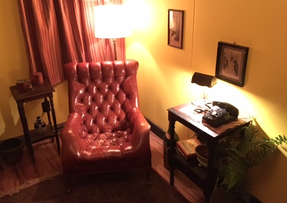 In-game: A large red leather chair in a 1950s livingroom. A rotary phone sits on an endtable beside it.