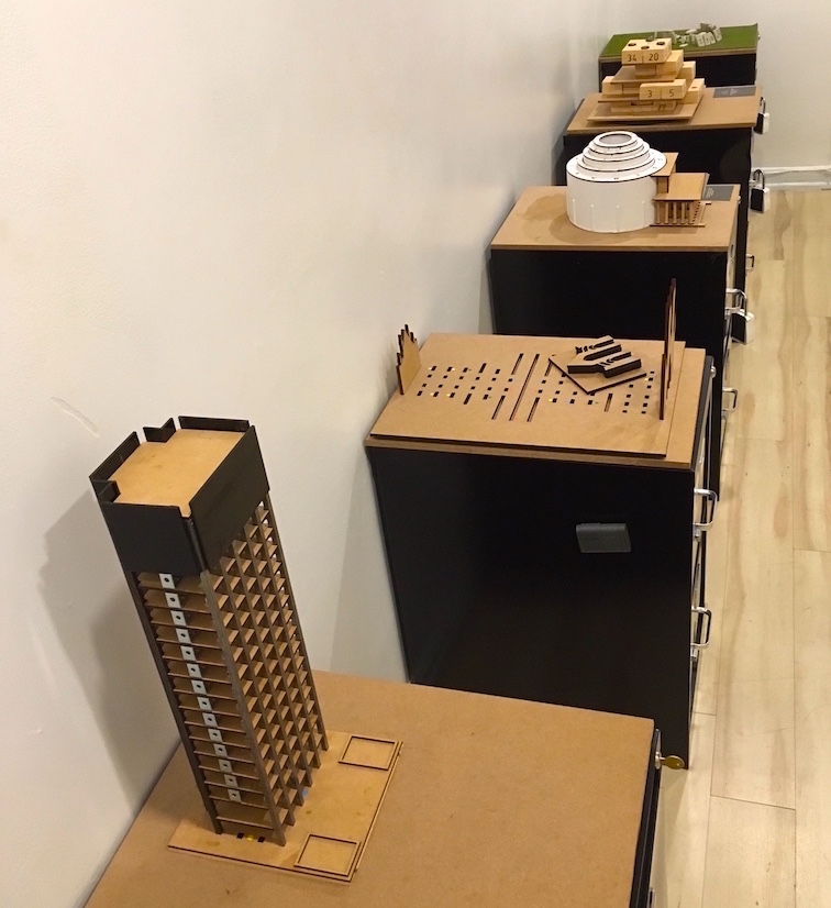 In-game: A series of filing cabinet pedestals, each with a different building model puzzle atop it.
