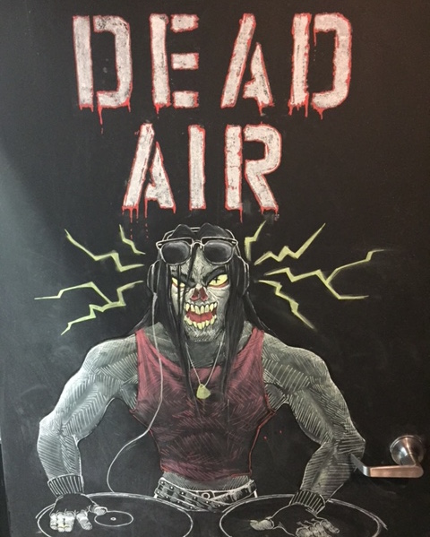 In-game: Door art of a zombie at a turntable. It reads "DEAD AIR"
