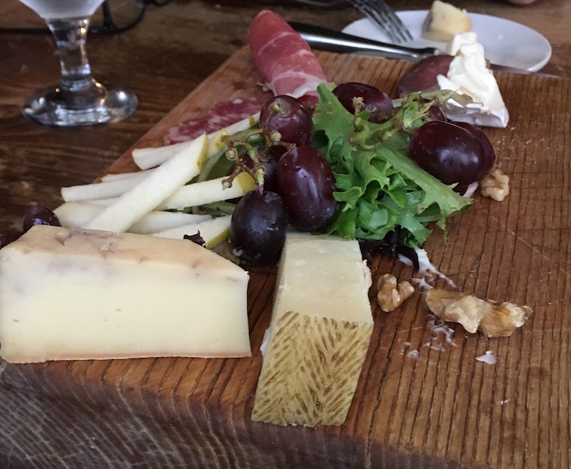 A have eaten plate of food including varies cheeses, greens, fruit, and meat.