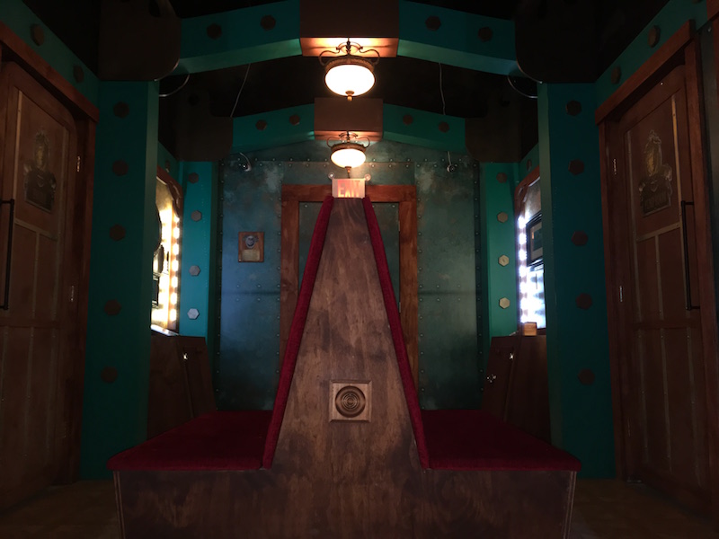 In game: The ornate interior of the vessel has a large bench in the middle and large copper doors with green walls covered in large rivets.