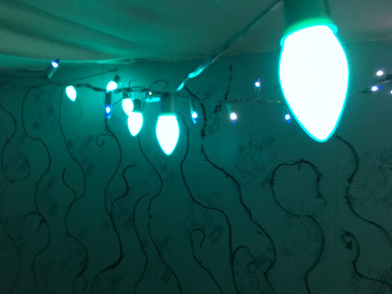 In game; blue Christmas lights illuminate the Upside Down as black tendrils cling to the walls.