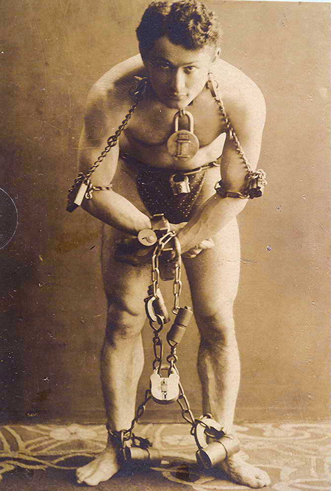 Harry Houdini bound by his wrists, ankles forearms, and neck in chains and many locks.