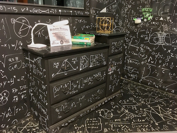 In-game: Black walls and furniture covered in white writing of mathematical symbols and equations. 