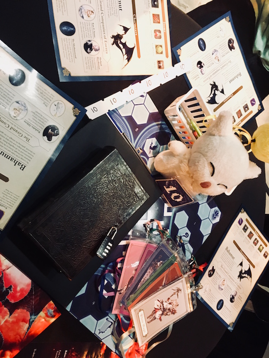 In-game: The initial table setup. There's a book sealed shut with a padlock, a Moogle doll, and an assortment of paper puzzle components.