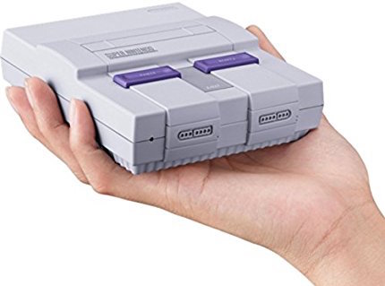 A hand holding the tiny Super Nintendo Classic in the palm of a hand.