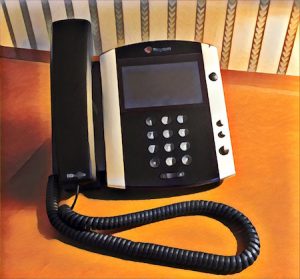 Vibrant filtered image of a Polycom telephone resting on a wood and leather desk.