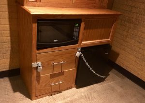 In-game: A seedy hotel mini-fridge, microwave, and dresser covered in padlocks.