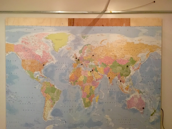 In-game: a world map covering a wall with black dots over select major cities.