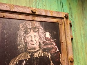 In-game: a portrait of a mad scientist framed with an oxidizing metal frame.