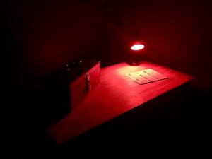 In-game: a dark room with a table lit red and a locked toolbox on top of it.