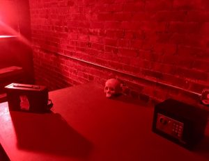 In-game: a large red lit table with a small sage, a skull, and a locked ammo box.