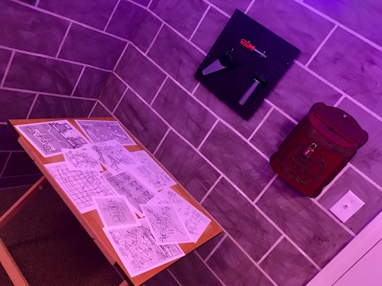 In-game: a drafting table with toy designs, mounted to the wall above are toy tools.