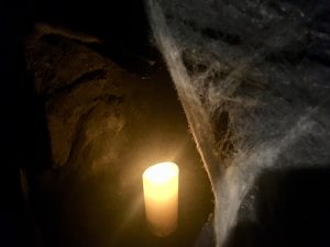 In-game: A dark cave with cobwebs and a glowing candle.