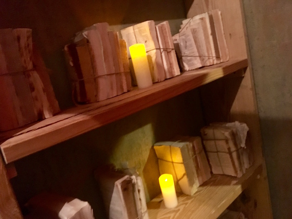 In-game: A wooden bookshelf covered in roped bundles of coverless books and glowing candles.