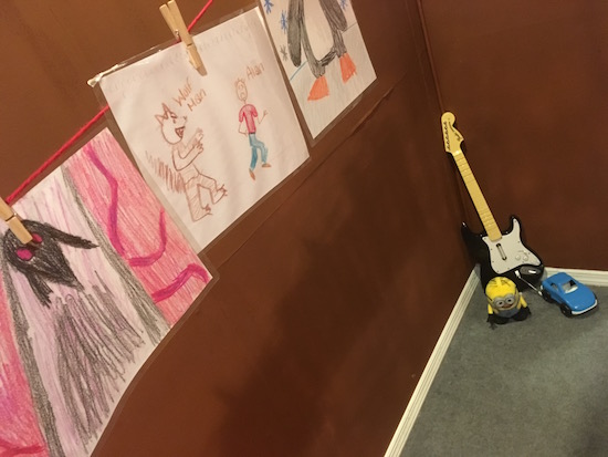 In-game: a string of child's art held up by clothespins, hanging over some kids toys.