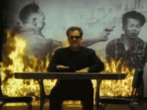 Billy Joel slapping his hands on a keyboard with a fire burning behind him.