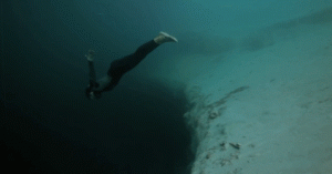 Skin diver swimming off into darkness and disappearing.