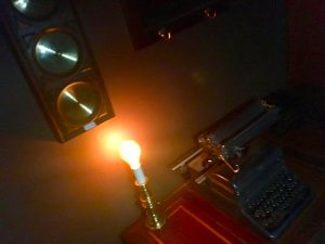 In-game: A typewriter beside an exposed glowing lightbulb in an otherwise dim room.