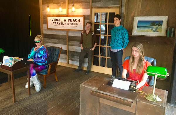 The travel agency's lobby with a woman dressed like she's from the 60s, a guy from the 70's, a woman from the 80s, and a guy from the 90s.