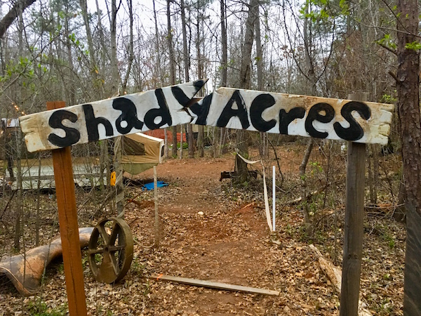 The entry way to The Shiners. A broken archway reads, "Shady Acres." Beyond is a wooded trailer park.