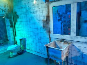 In-game: A rundown white tiled room with a big slop sink and a toilet.