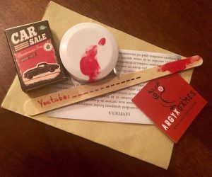 The Argyx Prelude gaming components including a matchbox, a bloody tape measure, a nail file labeled Youtube, and bible scripture.