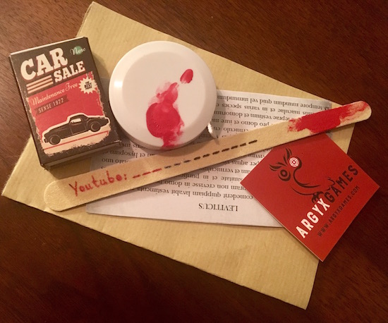 The Argyx Prelude gaming components including a matchbox, a bloody tape measure, a nail file labeled Youtube, and bible scripture. 