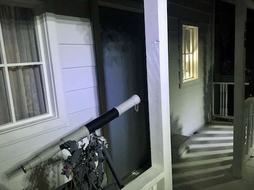 In-game: The front of a greyscale home with a telescope on the porch and a light on in the window.