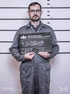 David's Prison Escape mugshot in an grey jump suit.