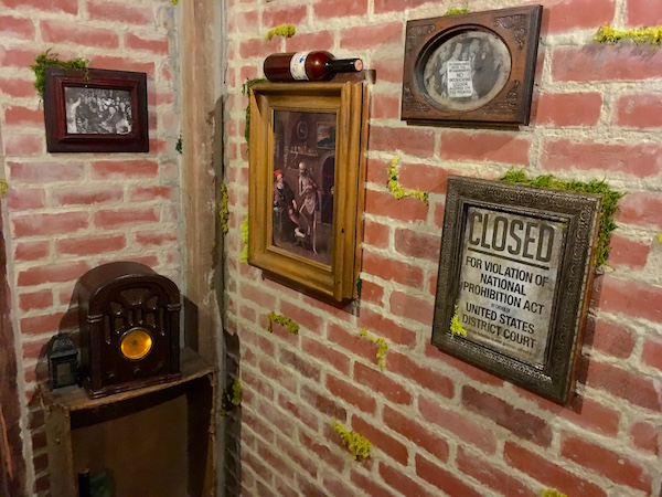 In-game: A corner of the brick wine cellar with a few photos, a bottle of wine, and an old radio.