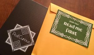 A green letter that reads "Part Two Read Me First," atop a sealed manila envelope and the Post Curious box.