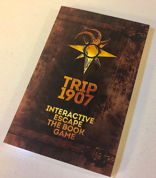 The faux leather cover of Trip 1907: Interactive Escape The Book Game features a gold compass rose with tentacles emerging from North.